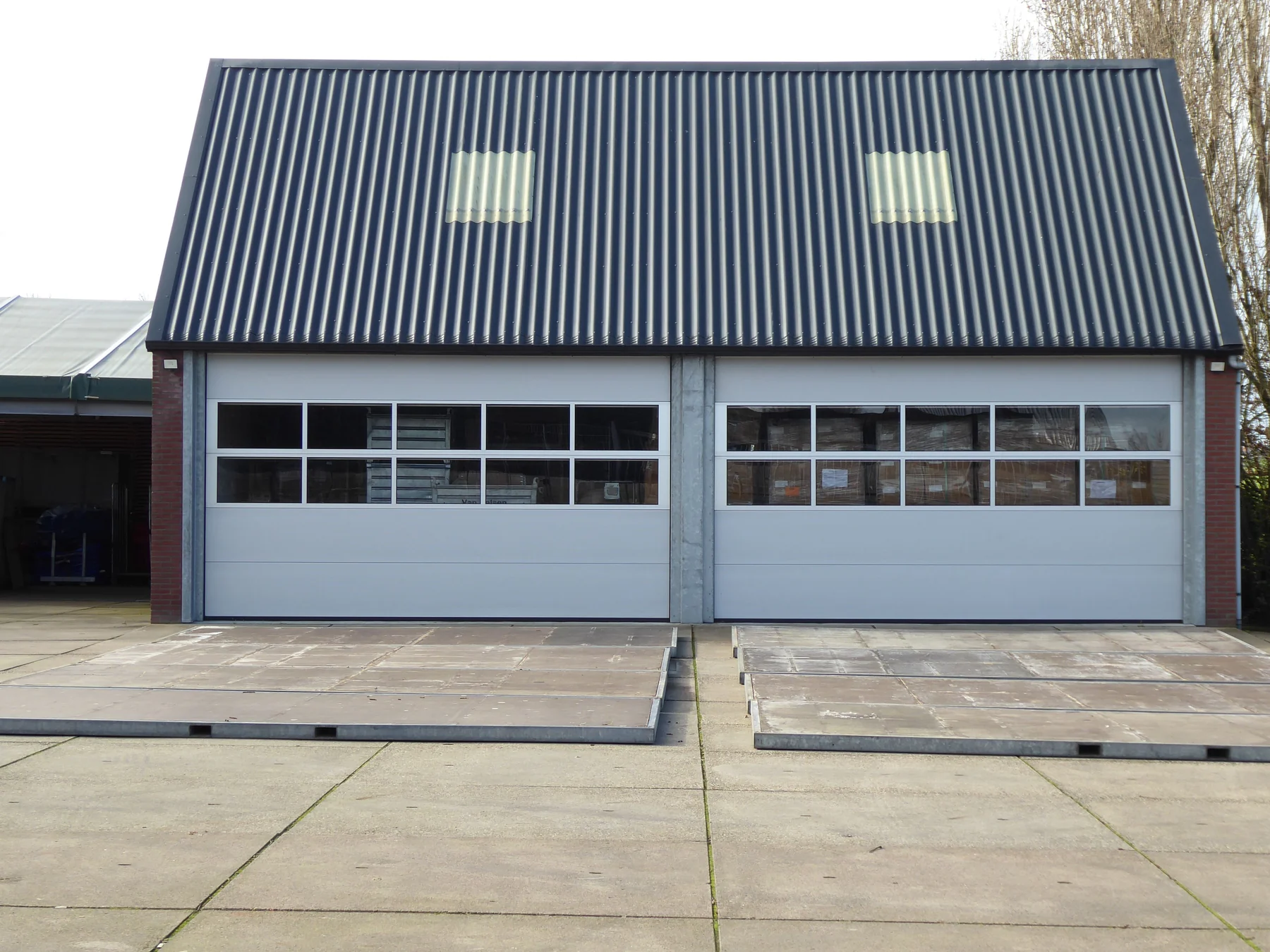 Illustrative photo of a detached garage-style workshop with a dark metal roof and two overhead doors