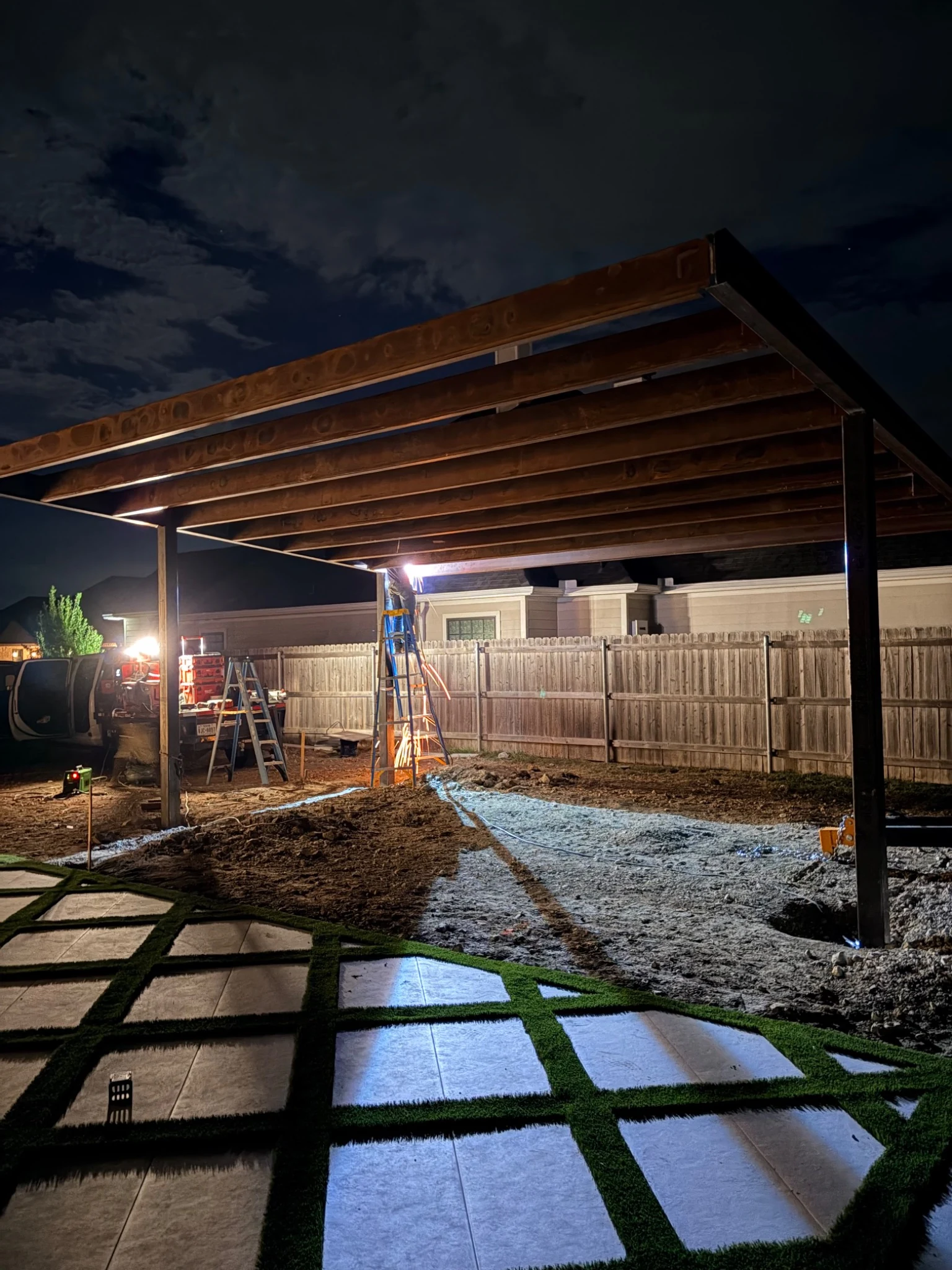 Company-supplied night photograph showing the cantilever patio-cover framing and patio footprint during installation
