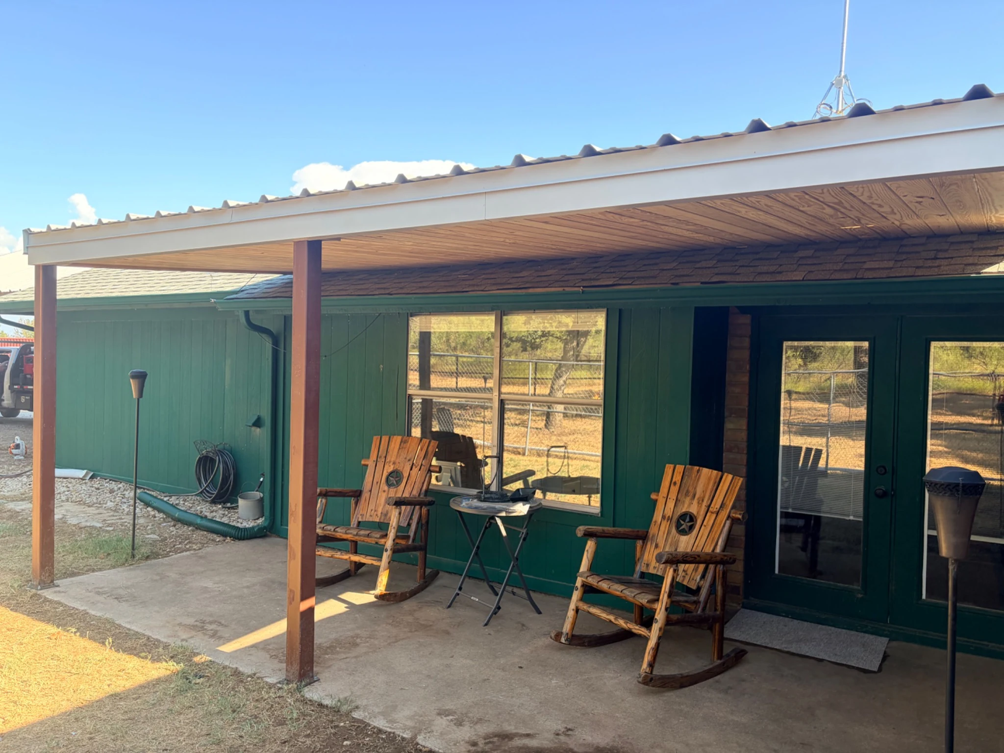 Company-supplied exterior photograph of a solid-roof patio cover with a wood-paneled underside by a green home