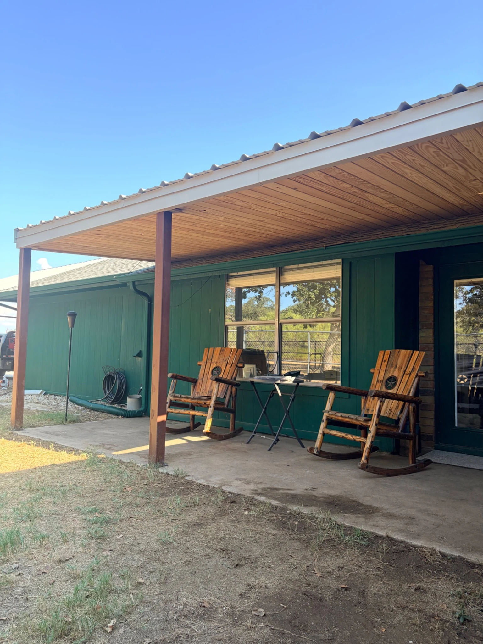 Company-supplied view of a patio cover with a light-colored roof, wood-paneled ceiling and supporting posts
