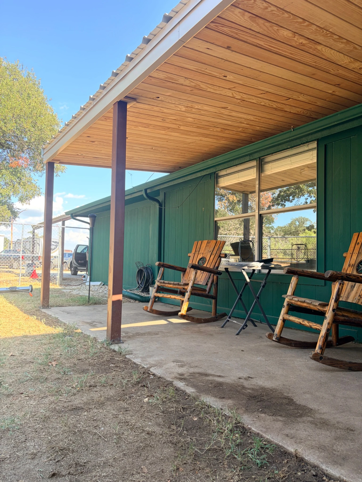 Company-supplied side view beneath a patio roof showing the wood-paneled underside and open garden edge
